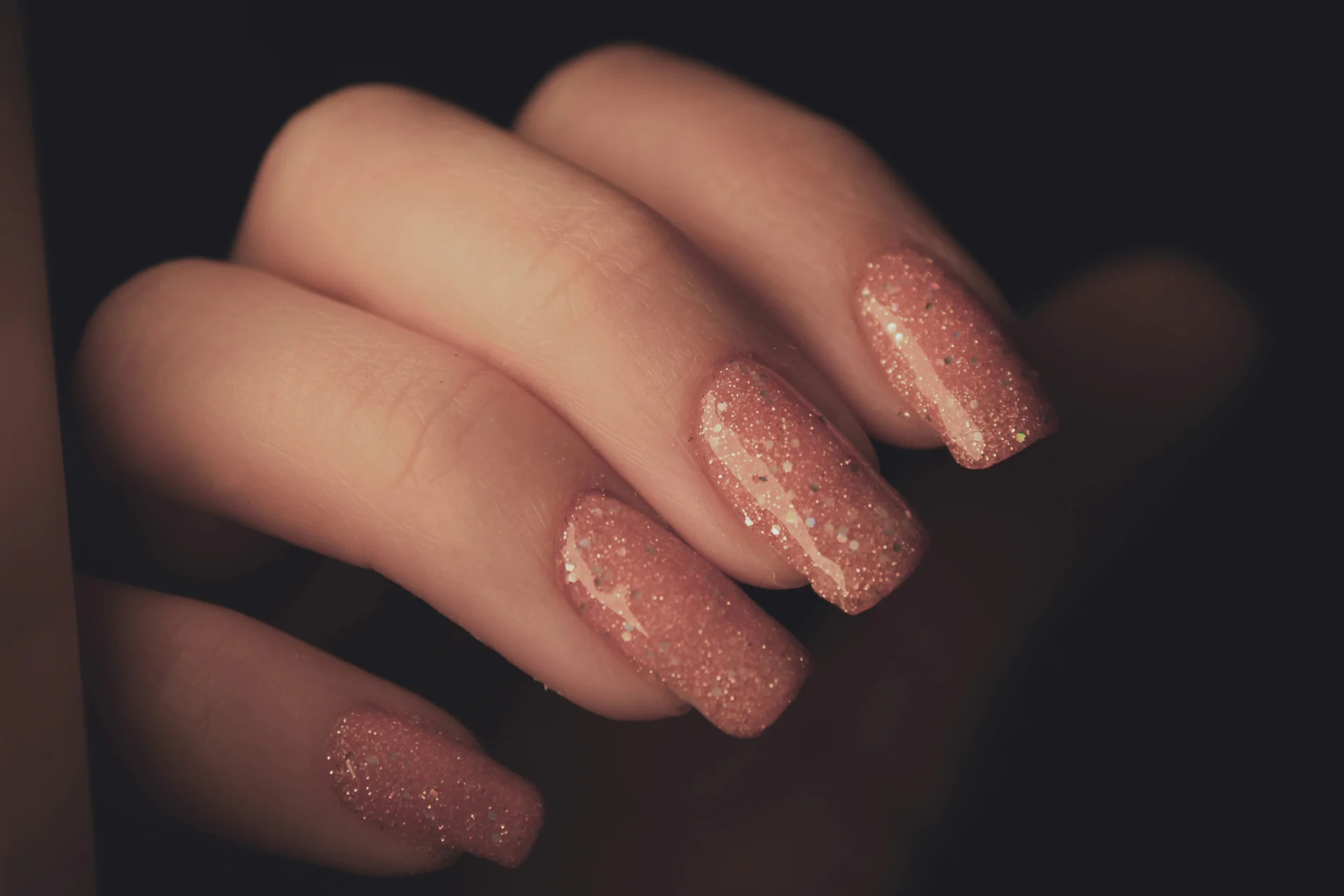 Zbliżenie na dłoń kobiety z zadbanymi paznokciami pomalowanymi na różowo, z widocznym manicure.