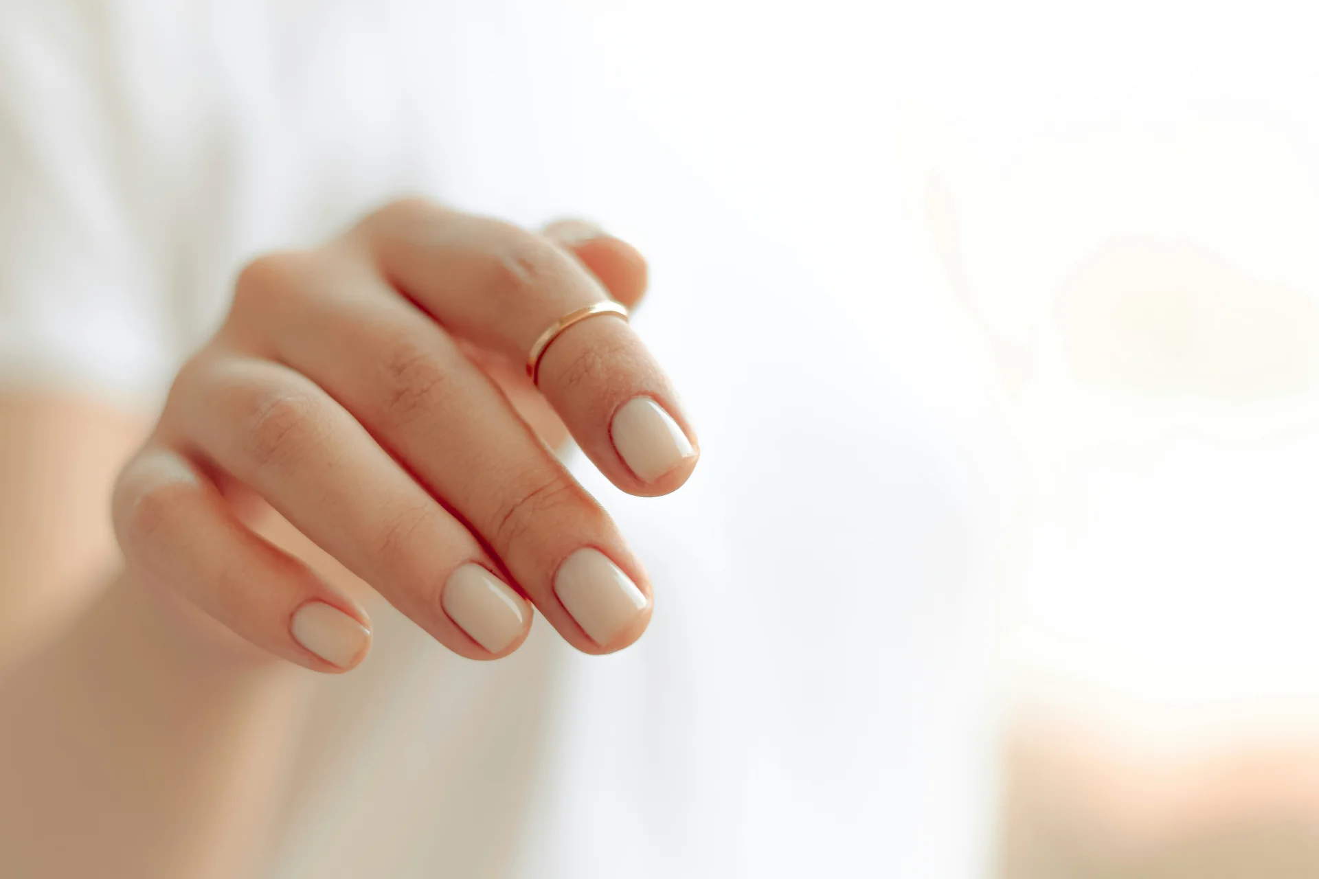 Zbliżenie na dłoń kobiety z eleganckim, białym manicurem, prezentującym zadbane paznokcie.