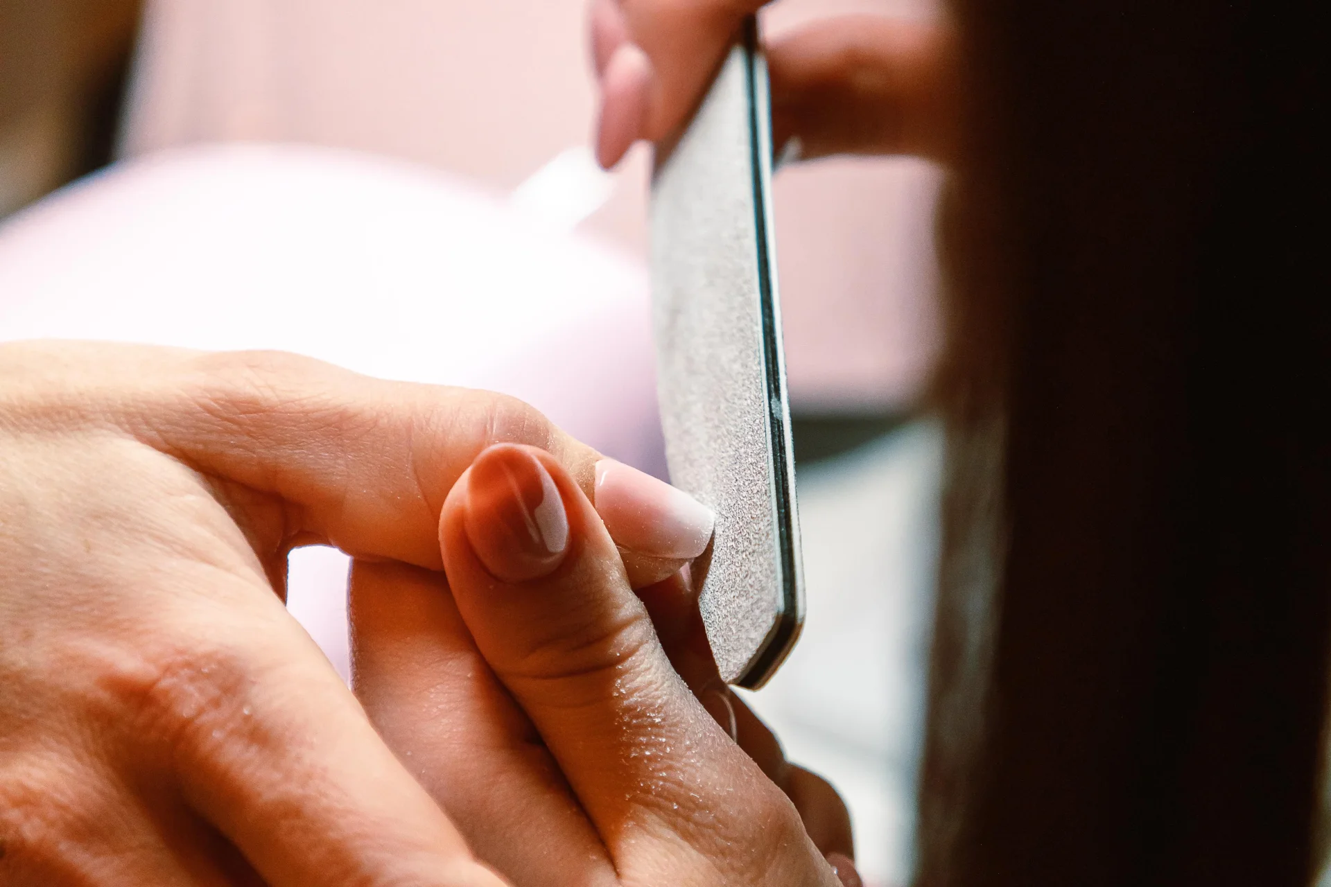 Zbliżenie na dłonie podczas profesjonalnego manicure, kosmetyczka używa pilnika do paznokci.